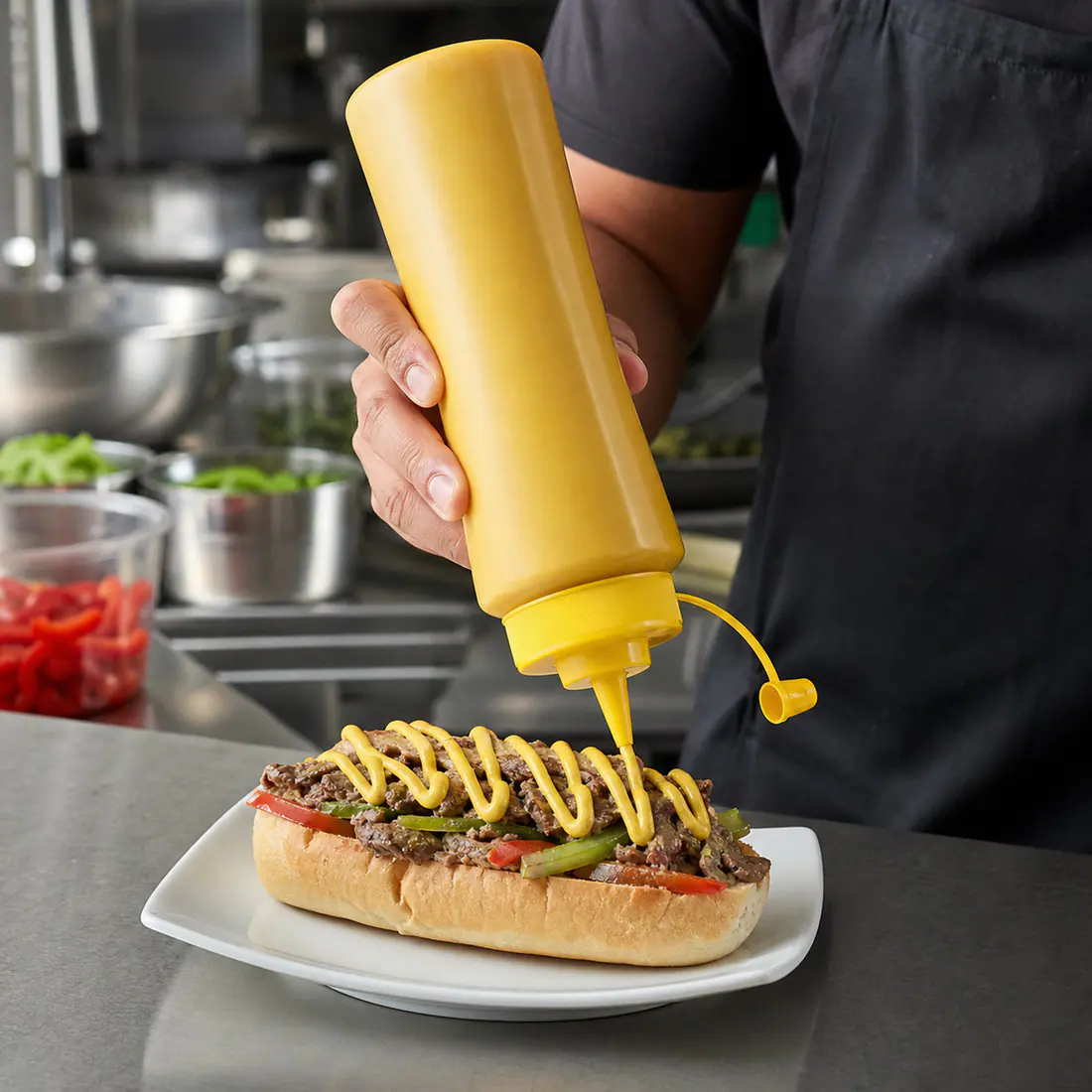 Cuisinier utilisant un flacon souple de sauce pendant le dressage d'un plat