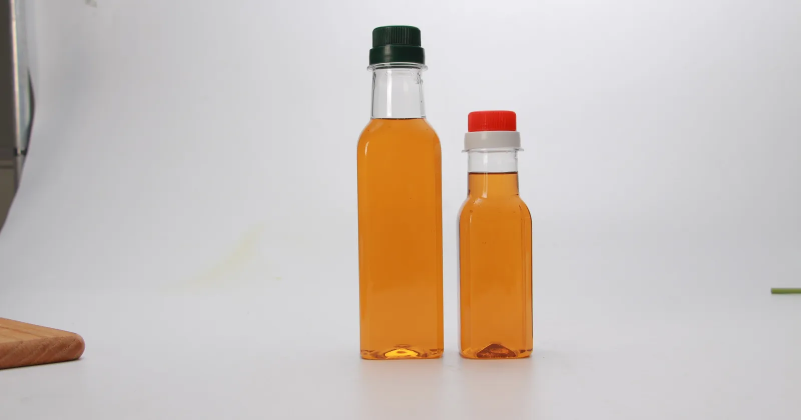 Deux bouteilles transparentes pour condiments avec fermetures de formats différents, verte et rouge