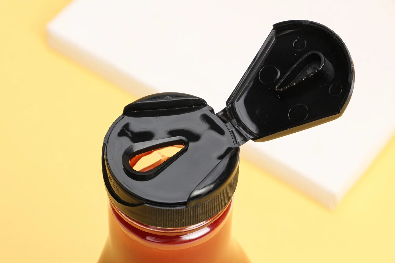 Gros plan d’une fermeture noire à clapet ouvert sur un flacon de sauce, avec son orifice de distribution